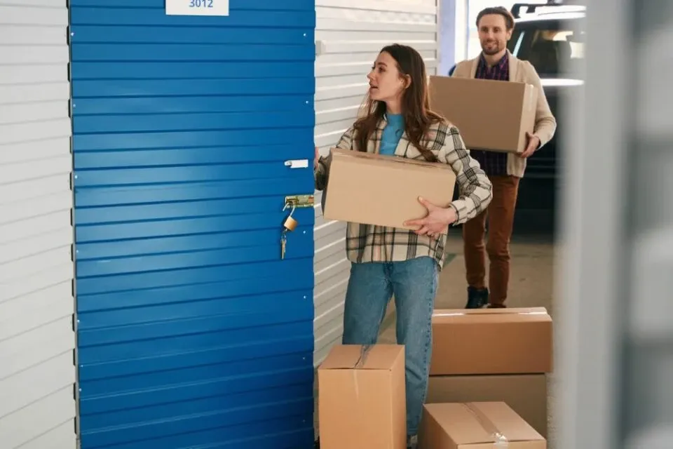 Young woman and man carrying boxes into storage unit