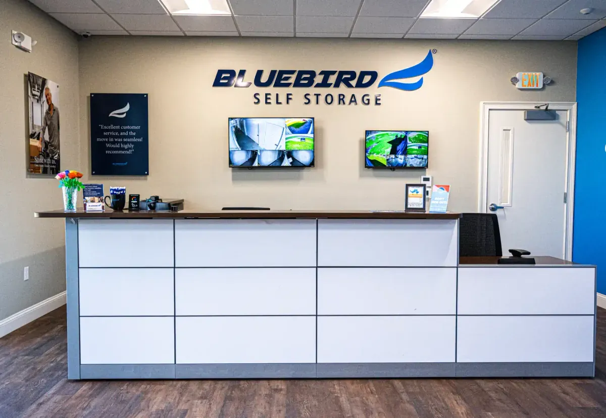 Bluebird Self Storage front desk with security monitors and branded logo on wall