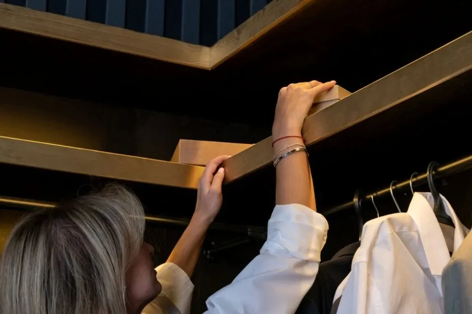 Woman reaching for items on high shelf in a closet.