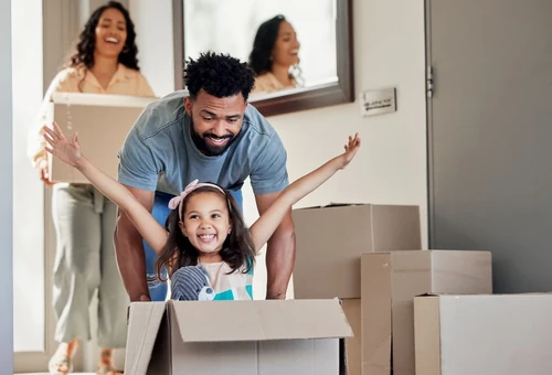 A family unpacking moving boxes in a new home, with parents and a child smiling while settling in together.