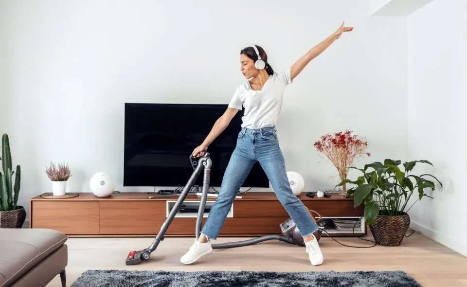Woman listening to music while cleaning the living room floor with a vaccum cleaner