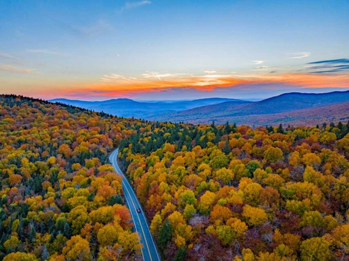 Aerial view of road in colorful autumn mountain forest during sunset