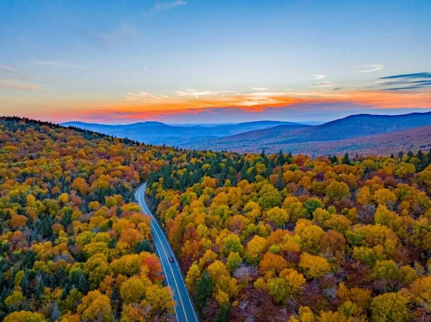 Aerial view of road in colorful autumn mountain forest during sunset