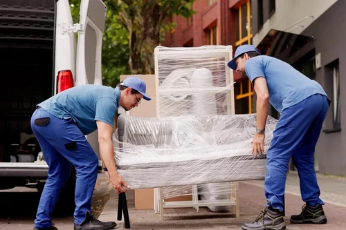 Two men lifting a couch that is prepped for storage into a moving turck.