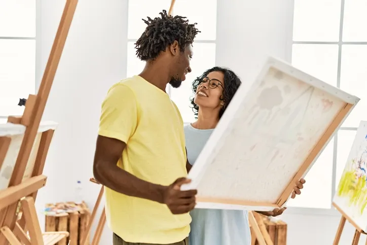 Couple smiling happy holding canvas at art studio.