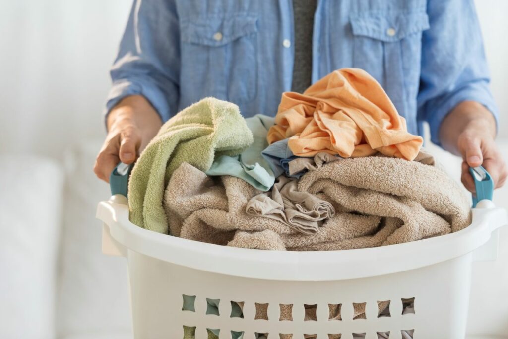 A man holding a white laundry hamper filled with towels and clothes.